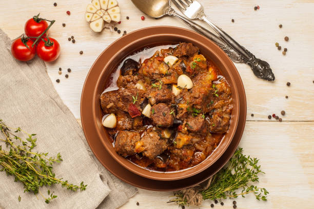 istock Braised meat with vegetables in a thick sauce. A large portion in a deep plate is ready to eat. Rustic decoration on a dark wooden background. 1205304380