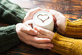 Couple holding hands around a mug of coffee with a cocoa heart on milk foam