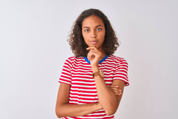 赤いストライプのtシャツを着た若いブラジル人女性は、孤立した白い背景の上に立ち、腕を組んで手をあごに上げて微笑むカメラに自信を持って見ていました。ポジティブに考える。 - front view female isolated on red happiness ストックフォトと画像