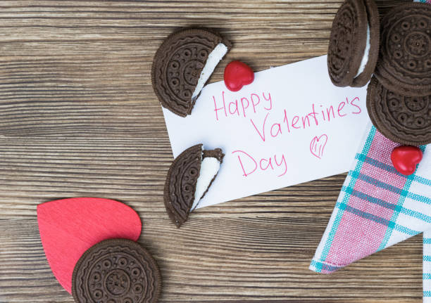 chocolate chip cookie sandwich on a colored napkin on a wooden background. wooden and red hearts. Happy Valentine's day. beautiful picture with biscuits. texture. chocolate chip cookie sandwich on a colored napkin on a wooden background. wooden and red hearts. Happy Valentine's day. beautiful picture with biscuits. texture. round sugar cookie stock pictures, royalty-free photos & images