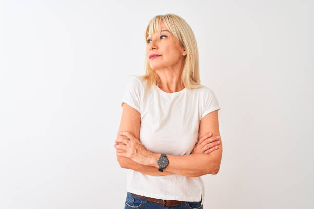 средний возраст женщина носить случайные футболку стоял над изолированным белым фоном глядя в сторону с скрещенными руками убежден и увер� - arms crossed стоковые фото и изображения