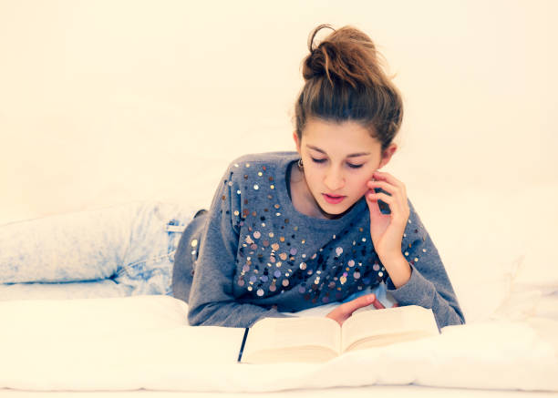 Carefree young girl reading a book on the bed