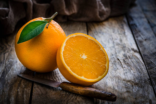Close up view of whole and sliced organic oranges on rustic wooden table. Predominant colors are orange and brown. High resolution 42Mp studio digital capture taken with Sony A7rii and Sony FE 90mm f2.8 macro G OSS lens