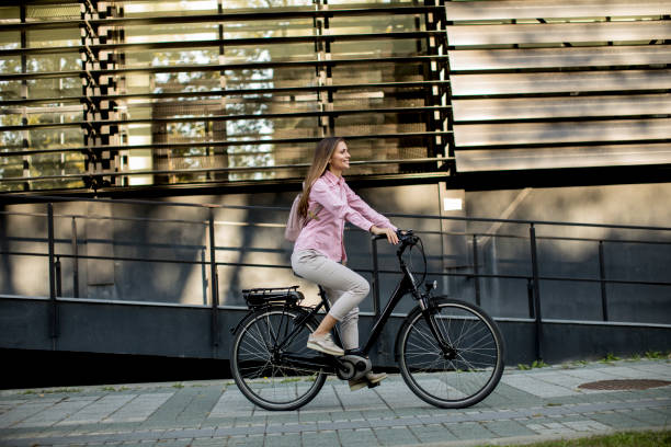 Young woman riding e bike in urban enviroment Young woman riding e bike in urban enviroment at sunny day electric bicycle photos stock pictures, royalty-free photos & images