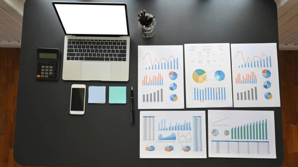 istock Business equipment/accessories putting on the modern working desk. Flat lay white blank screen laptop, smartphone, calculator, pencil holder, post-it and graphic chart on the black table. 1205310390