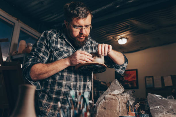 istock Bearded man works in a pottery workshop, concentrating on the process of creating a clay cup 1205314913
