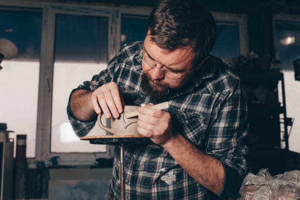 istock Bearded man works in a pottery workshop, concentrating on the process of creating a clay cup 1205314931