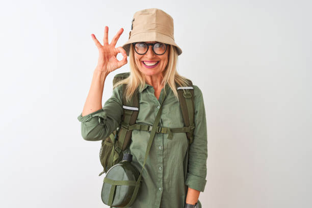 istock Middle age hiker woman wearing backpack hat canteen glasses over isolated white background smiling positive doing ok sign with hand and fingers. Successful expression. 1205315618