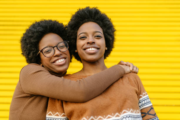 portret van gelukkige tweelingzusters voor gele achtergrond - eeneiige tweeling stockfoto's en -beelden
