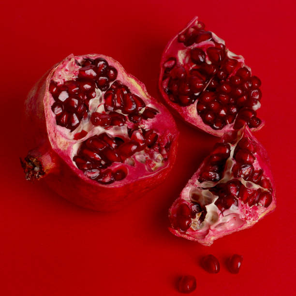 istock Red pomegranate isolated on red background. Pomegranate seeds on a red background. Pieces of pomegranate are scattered. Square . Copy space for text. 1205317585