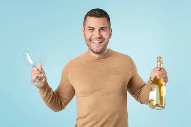 Photo of Happy man holding goblets and champagne bottle over blue background