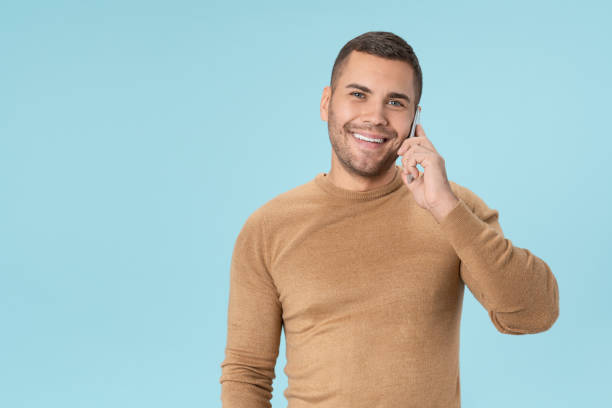 istock Cheerful young man in casual talking on mobile phone posing isolated on blue background 1205327348