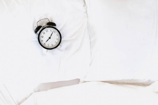 istock Alarm clock in bed. Overslept or bed time concept 1205328406