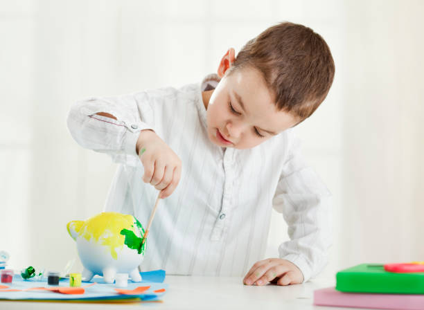 istock Boy painting piggy bank 1205335106