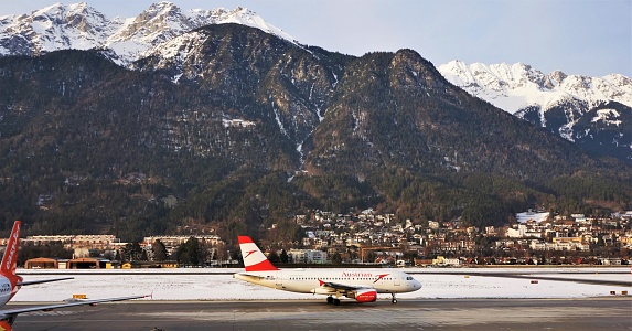 Innsbruck, Austria - 8 February 2020: An aircraft is taxi-ing along the apron before heading to the runway at Innsbruck Airport. There is a covering of snow beside the runway. Mountains rise sharply beyond the urban area on the far side of the valley.