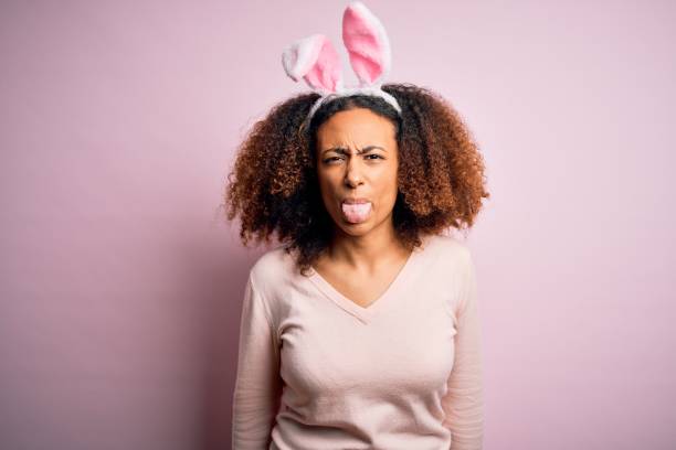 jeune femme afro-américaine avec des oreilles de lapin afro utilisant au-dessus du fond rose collant la langue dehors heureuse avec l’expression drôle. concept d’émotion. - easter rabbit bizarre women photos et images de collection