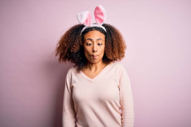 jeune femme afro-américaine avec des oreilles de lapin afro utilisant au-dessus du fond rose faisant le visage de poisson avec des lèvres, le geste fou et comique. drôle d’expression. - easter rabbit bizarre women photos et images de collection