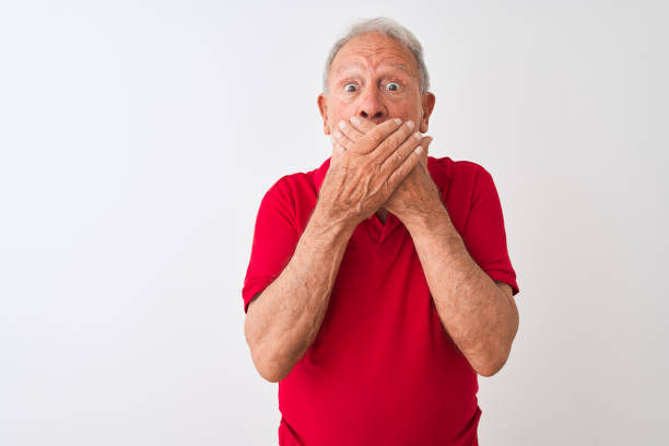 istock Senior grey-haired man wearing red polo standing over isolated white background shocked covering mouth with hands for mistake. Secret concept. 1205342840