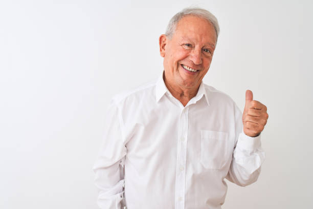 istock Senior grey-haired man wearing elegant shirt standing over isolated white background doing happy thumbs up gesture with hand. Approving expression looking at the camera showing success. 1205342930