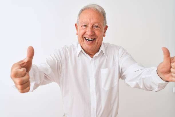 istock Senior grey-haired man wearing elegant shirt standing over isolated white background approving doing positive gesture with hand, thumbs up smiling and happy for success. Winner gesture. 1205342945