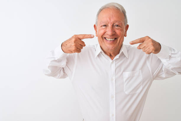 istock Senior grey-haired man wearing elegant shirt standing over isolated white background smiling cheerful showing and pointing with fingers teeth and mouth. Dental health concept. 1205343067