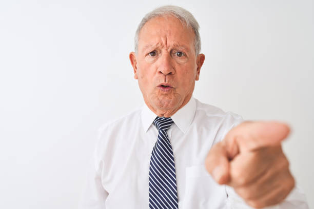 istock Senior grey-haired businessman wearing tie standing over isolated white background pointing with finger to the camera and to you, hand sign, positive and confident gesture from the front 1205343320