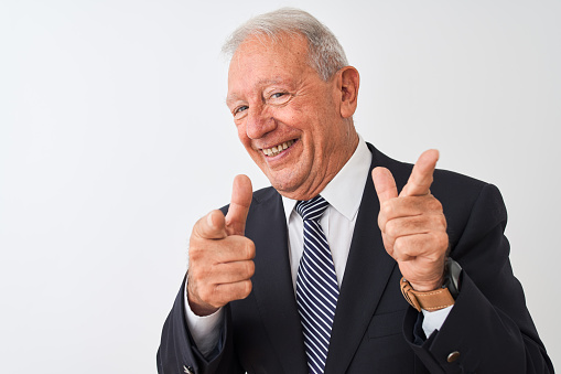 Senior grey-haired businessman wearing suit standing over isolated white background pointing fingers to camera with happy and funny face. Good energy and vibes.