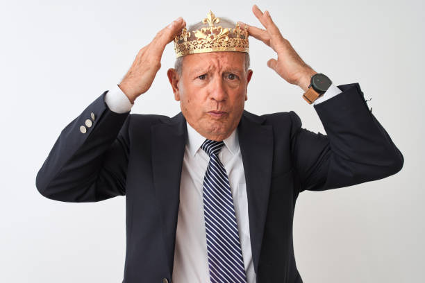istock Senior grey-haired businessman wearing crown king over isolated white background suffering from headache desperate and stressed because pain and migraine. Hands on head. 1205344804