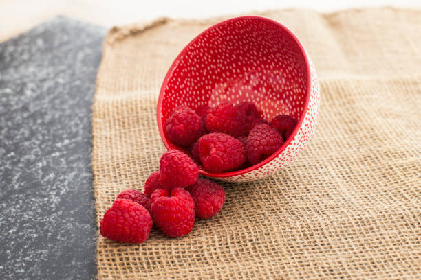 istock Red Raspberries in a ceramic plate in a black and rattan background 1205344955