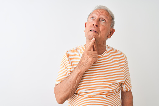 Senior grey-haired man wearing striped t-shirt standing over isolated white background Thinking concentrated about doubt with finger on chin and looking up wondering