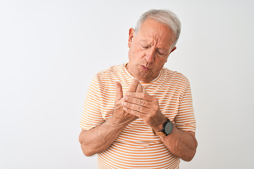 Senior grey-haired man wearing striped t-shirt standing over isolated white background Suffering pain on hands and fingers, arthritis inflammation