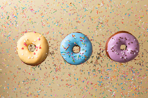 Colorful Donuts flying on yellow background. Sweet food background.