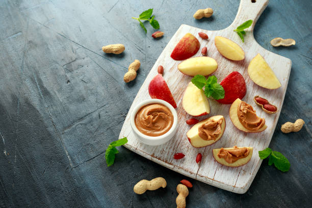 istock Peanut butter and apple to snack. on white wooden board 1205348562