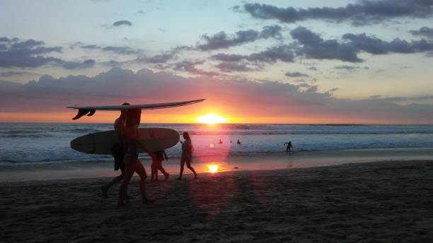 Beach Sunset With Surfers Beach Sunset in Santa Teresa Costa Rica with people walking and in the water costa rican sunset stock pictures, royalty-free photos & images