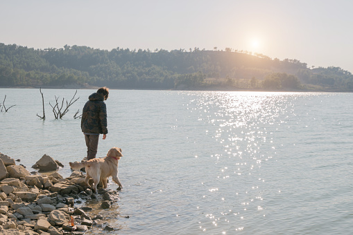 A teenage boy and his dog on the edge of a mountain lake in the fall