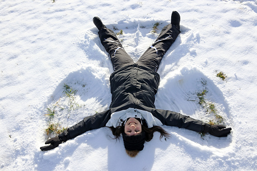 A young woman makes a snow angel in the winter snow