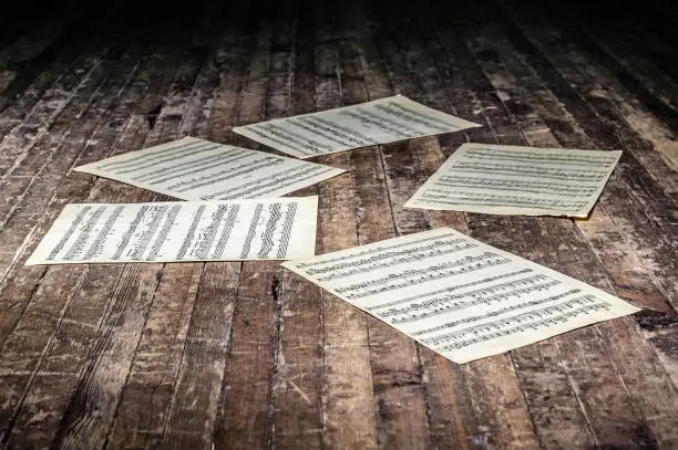 Photo of music sheets with notes of a musical work lie on the old floor in the dark