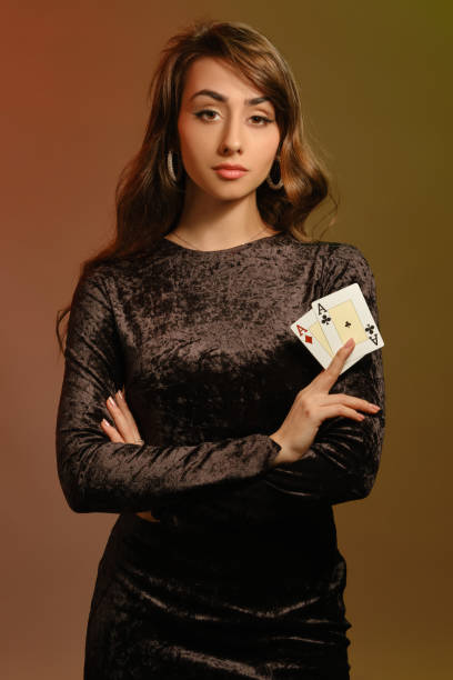 brunetka kobieta w czarnej aksamitnej sukience i biżuterii pokazującej dwa asy, pozując na kolorowym tle studia. hazard, poker, kasyno. zbliżenie - casino black and white gambling chip gambling zdjęcia i obrazy z banku zdjęć