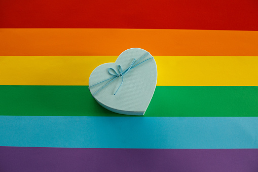 Directly above shot of of a gay rainbow as a background and a blue heart shaped Valentine's day gift box flat lay on top.