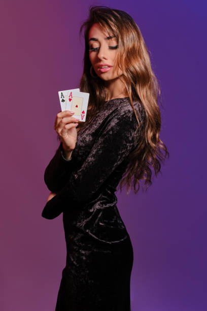brunetka dziewczyna w czarnej aksamitnej sukience pokazującej dwie karty do gry, pozując bokiem na kolokowym tle. rozrywka hazardowa, poker, kasyno. zbliżenie - casino black and white gambling chip gambling zdjęcia i obrazy z banku zdjęć