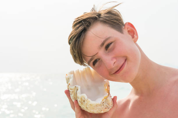 istock Young boy holding shell against sea 1205371623