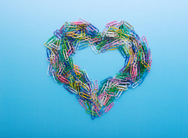 Multicolored paper clips arranged into in the shape of a heart on blue background.