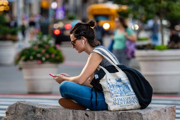 na skraju ulicy, kobieta siedzi na kamieniu i słucha muzyki ze smartfona, rozmyte pejzaż miejski w tle, nowy jork, usa - at the edge of audio zdjęcia i obrazy z banku zdjęć