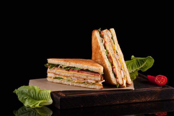 foto de um sanduíche de clube feito de peru, bacon, presunto, tomate, queijo, salada e decorado com duas metades de tomate cereja - sandwich club sandwich ham turkey - fotografias e filmes do acervo