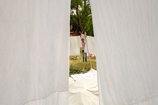 Delhi, India - April 22, 2017: Man hangs white sheets to dry on clotheslines on a large field in Delhi.