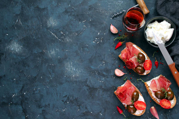 Bruschetta set for wine. Variety of small sandwiches with prosciutto, tomato and light cheese served with red wine on dark background. stock photo