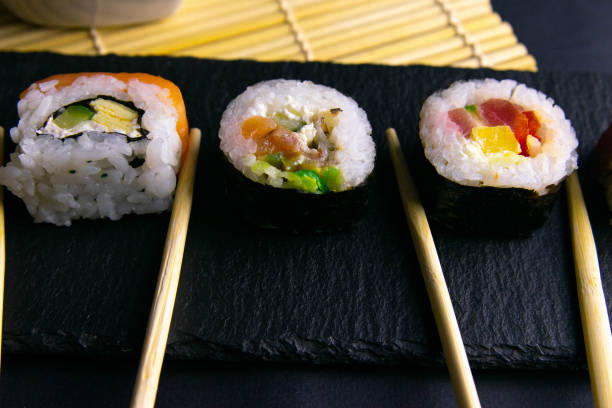 istock Sticks hold rolls that stand on a black graphite board for sushi that stands on a black background and a roll for a sushi spin 1205380370