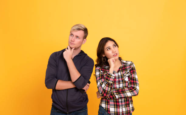 istock Young people man and woman thinking and touching chin while looking aside isolated over yellow background. 1205392436