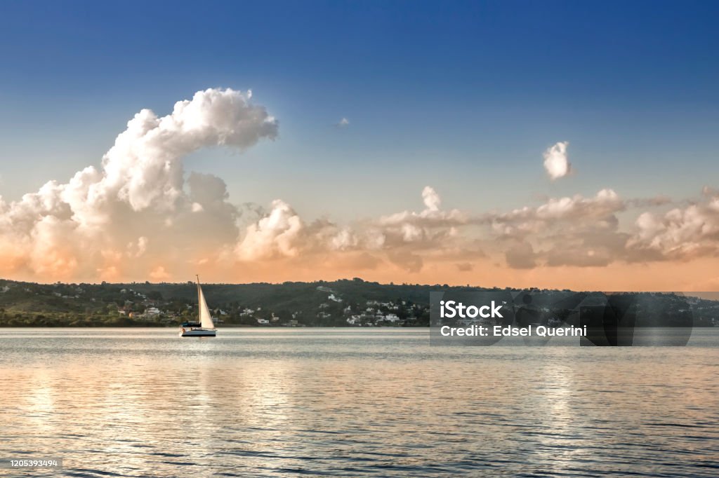 Sailboat in waters of Lake San Roque at sunset, Villa Carlos Paz, Cordoba, Argentina. Landscape of San Roque lake at sunset with a sailboat, Villa Carlos Paz, Córdoba province, Argentina. Argentina Stock Photo