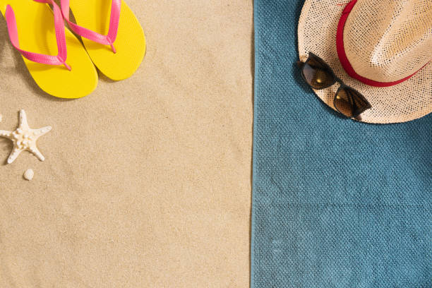 Summer vacation composition. Flip flops, hat and sunglasses on sand background. Travel vacation concept. Summer background. Border composition made of towel stock photo